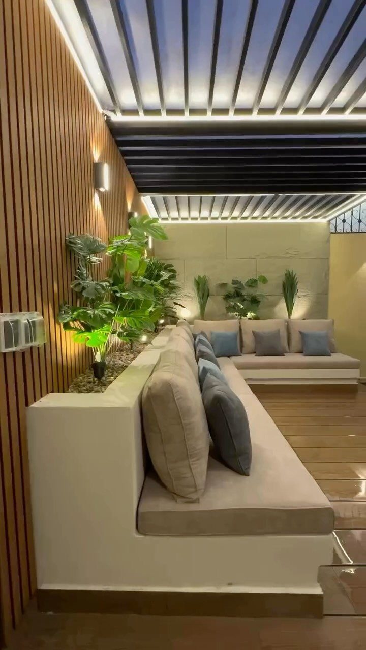 11 Around Deck Landscaping Ideas with Photos and Tips 6 Modern outdoor lounge with built-in seating, large green plants, and warm accent lighting.
