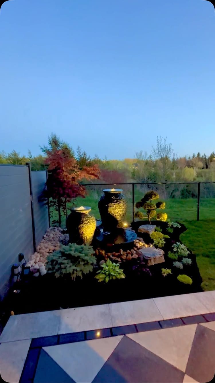 11 Around Deck Landscaping Ideas with Photos and Tips 7 A landscaped garden bed with dark mulch, green shrubs, and two dark ceramic water fountains.