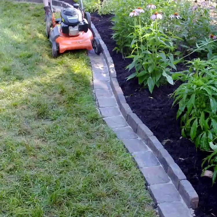 11 Around House Landscaping Ideas for Foundation to Fence 8 A lawn mower trims grass beside a curved garden bed lined with grey stone pavers.