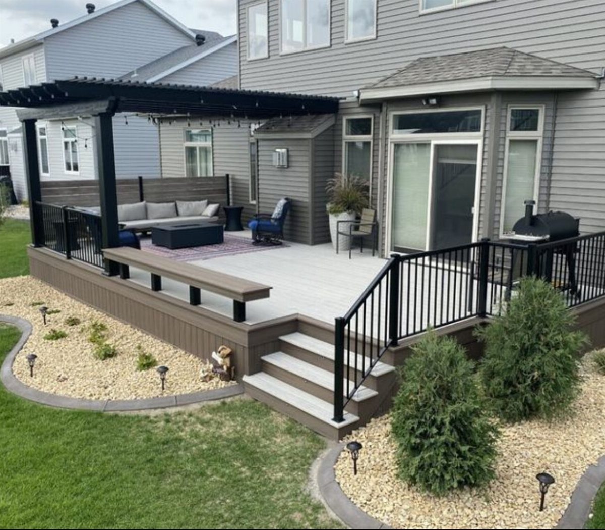 21 Backyard Deck Ideas For Any Size Space 10 Large multi-level wooden deck with grey planks, black railings, and a pergola attached to a grey house.
