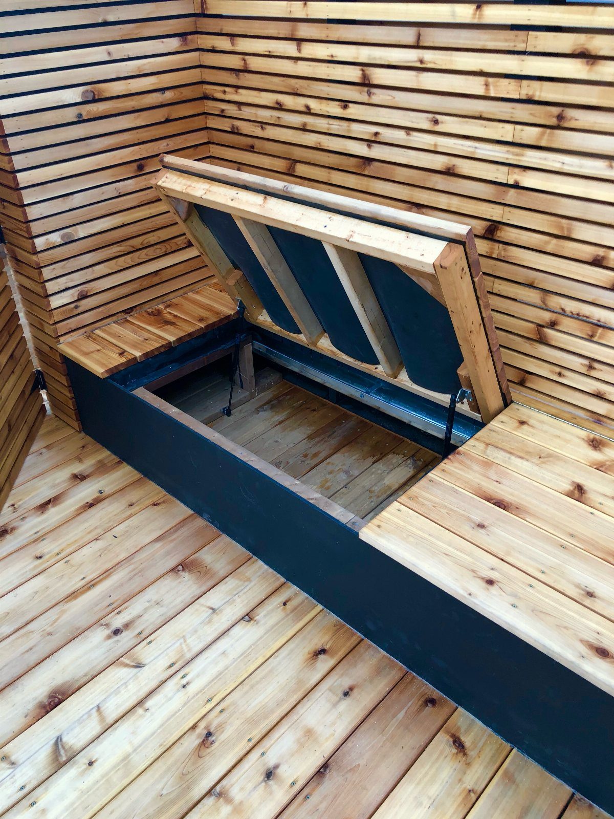 21 Backyard Deck Ideas For Any Size Space 20 An open wooden storage compartment built into a deck bench with light wood slats.
