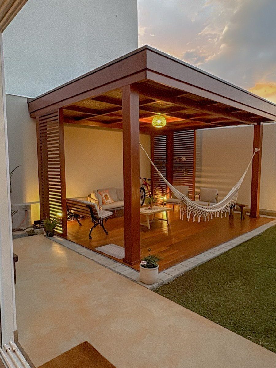 21 Backyard Deck Ideas For Any Size Space 18 A wooden outdoor deck structure featuring a white hammock, seating, and warm lighting at sunset.