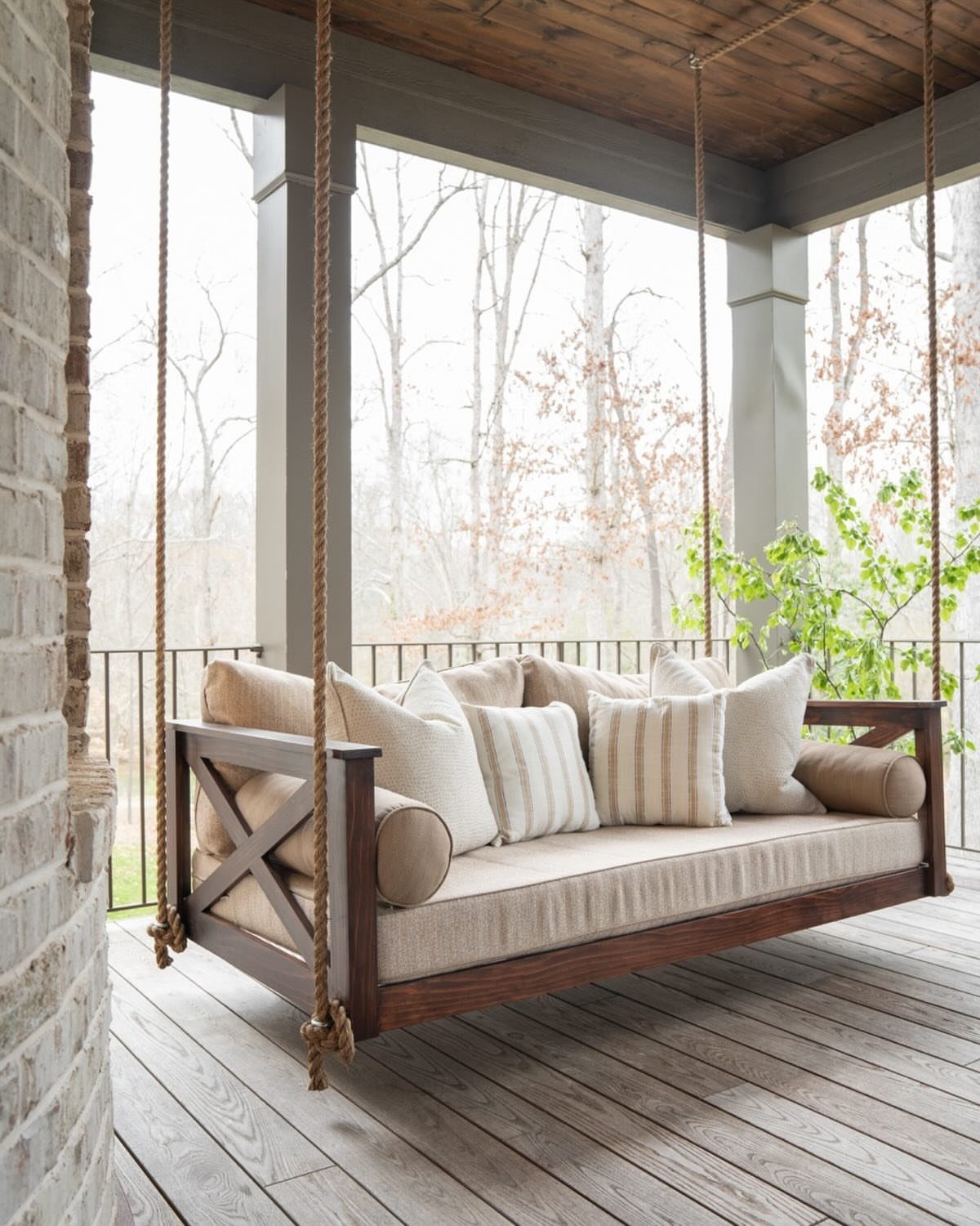21 Backyard Deck Ideas For Any Size Space 3 A wooden hanging porch swing bed with beige cushions and pillows on a wooden deck.