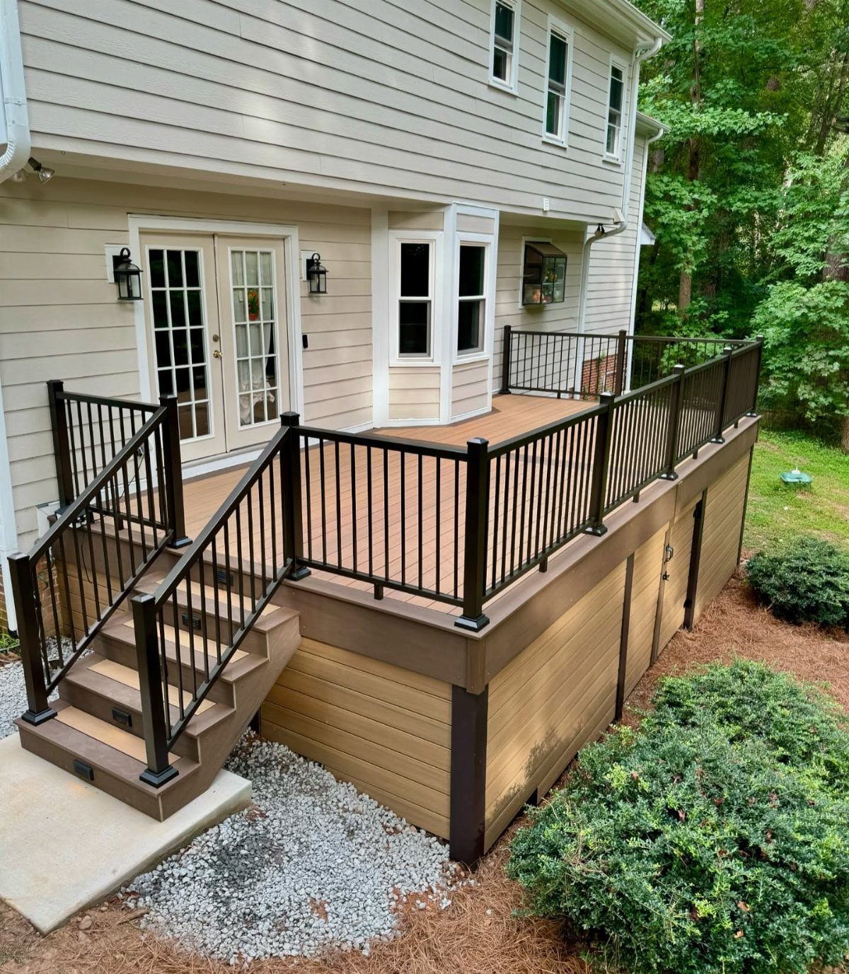 21 Backyard Deck Ideas For Any Size Space 14 A large wooden deck with dark brown railings and light tan decking attached to a house.
