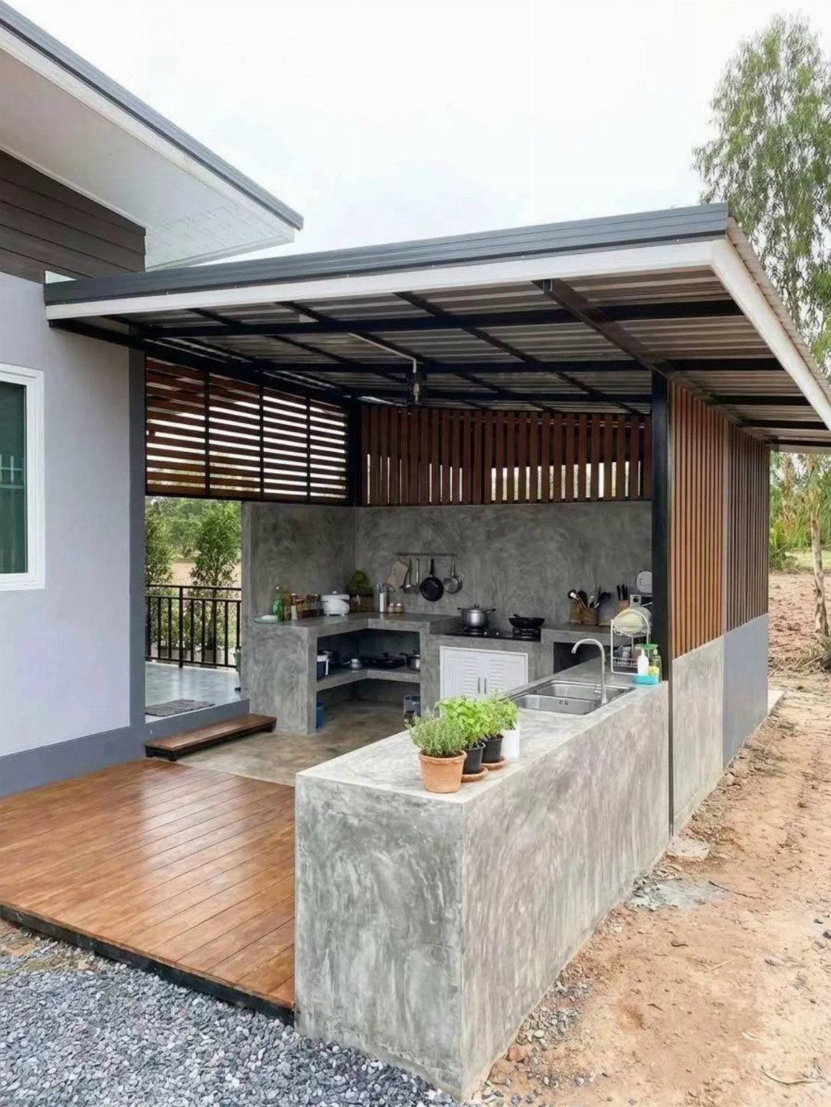 21 Backyard Deck Ideas For Any Size Space 12 Modern concrete outdoor kitchen with a sink and stovetop under a dark metal roof structure.