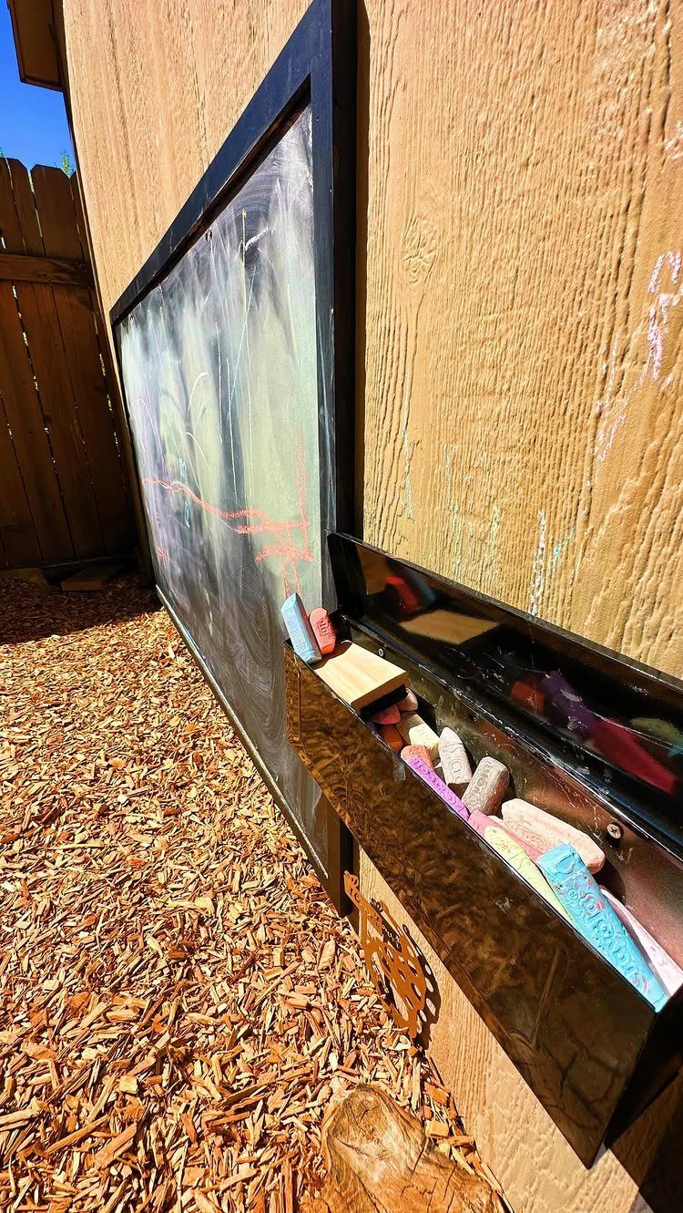 A large black-framed chalkboard mounted on a wooden wall with colorful chalk in a holder below.