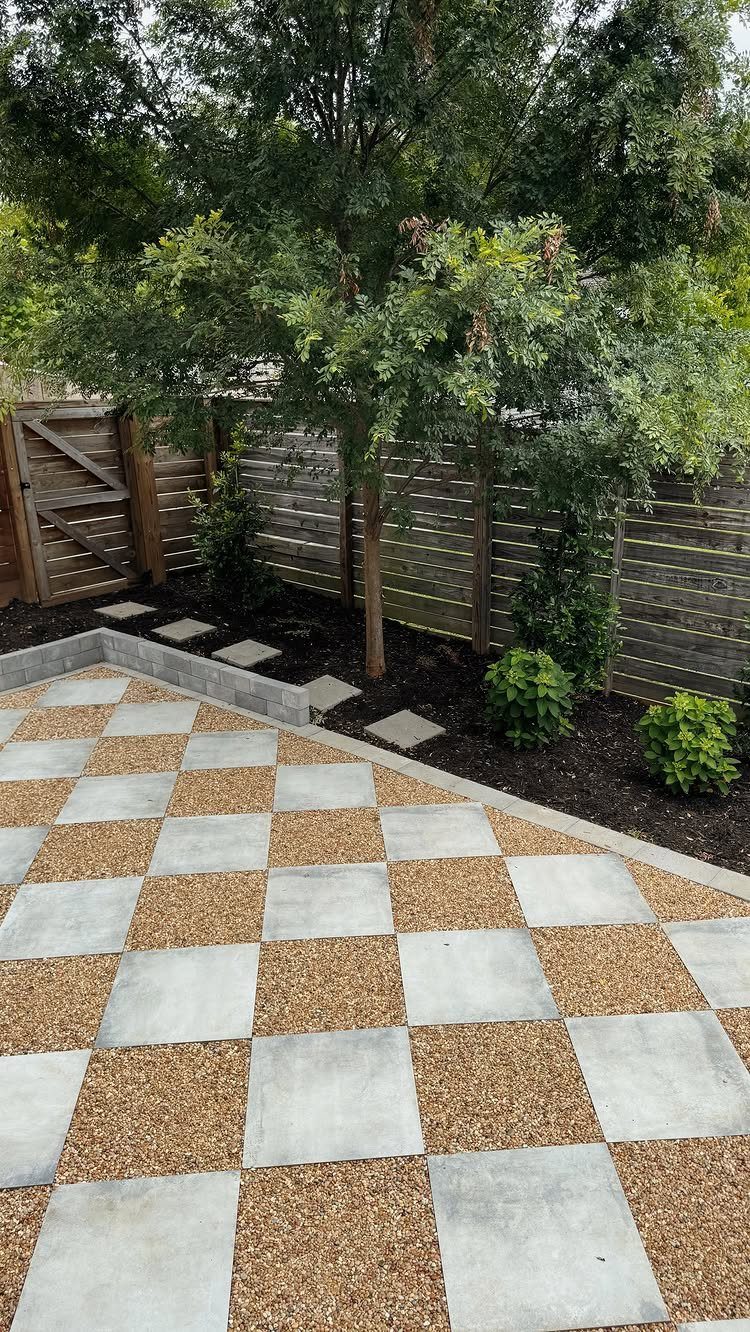 A checkerboard patio featuring alternating light grey concrete tiles and tan pea gravel squares.