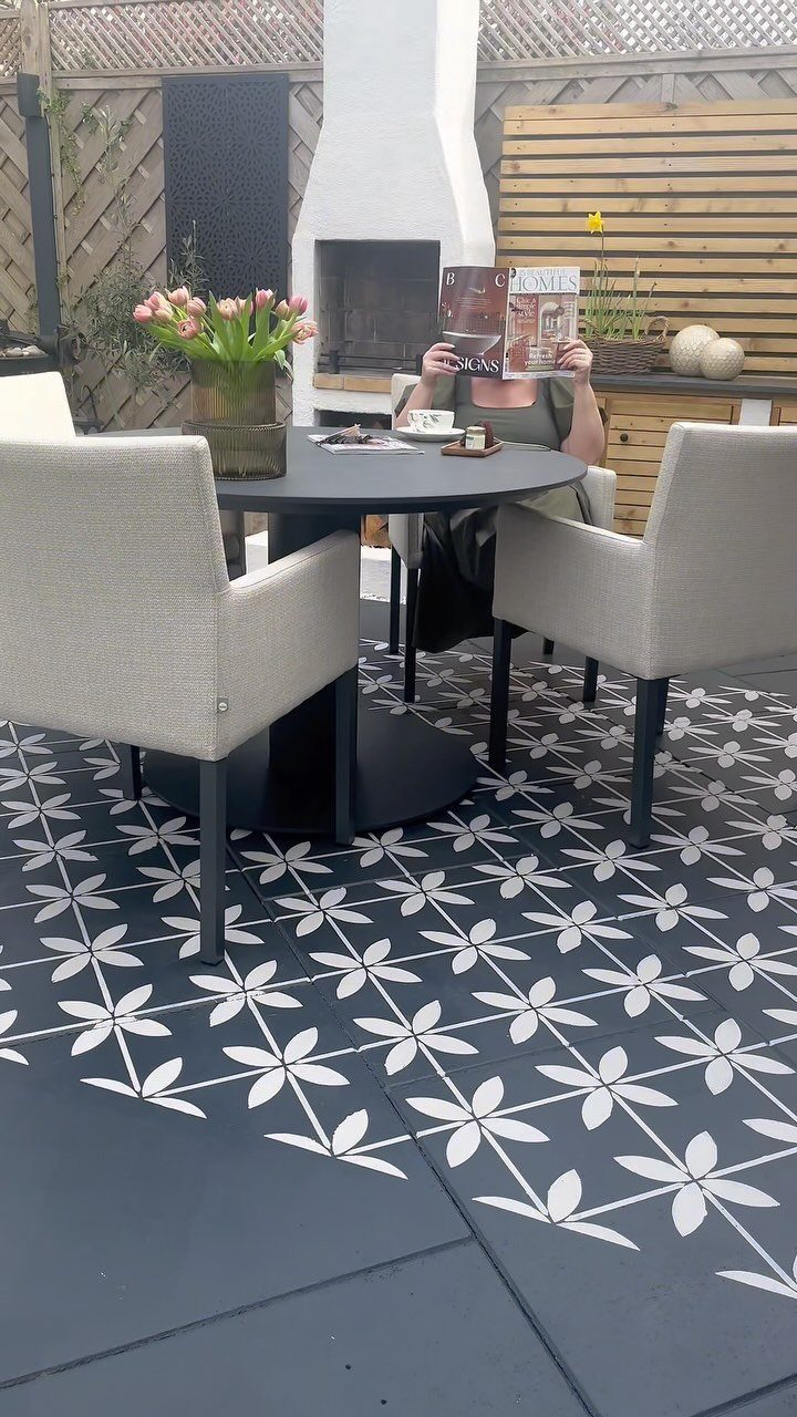Dark grey patio tiles with a large white stenciled floral pattern under outdoor dining furniture.