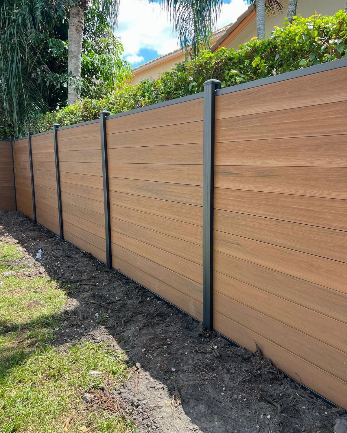 7 Backyard Fence Ideas for Privacy and Style 3 Horizontal composite privacy fence with dark grey posts installed in a backyard garden setting.