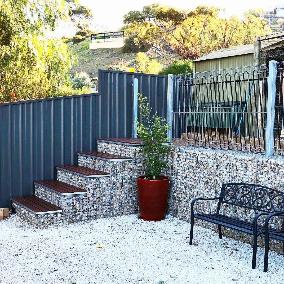 7 Backyard Fence Ideas for Privacy and Style 6 Stone-filled gabion wall forming steps and a retaining wall in a backyard setting.