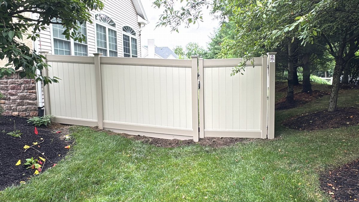 7 Backyard Fence Ideas for Privacy and Style 4 A light beige vinyl privacy fence installed in a green backyard next to a house.