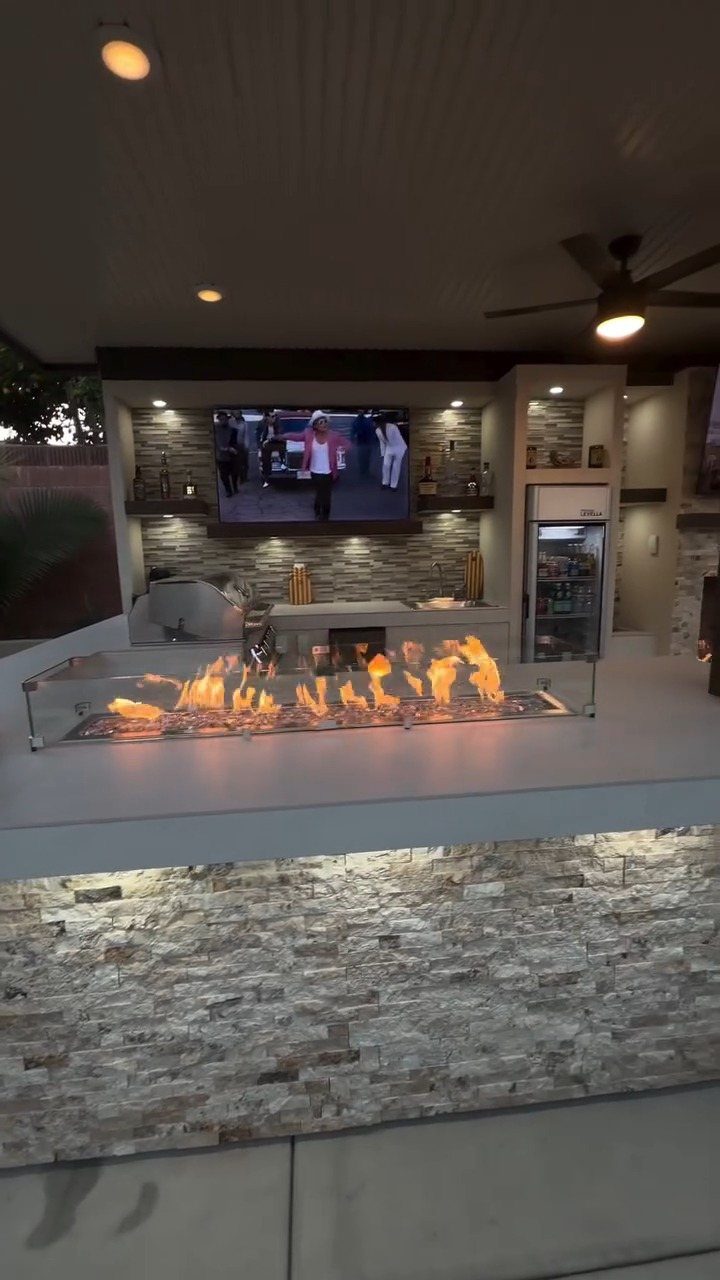 Gas fire pit flames on a stone counter in a modern outdoor kitchen area.