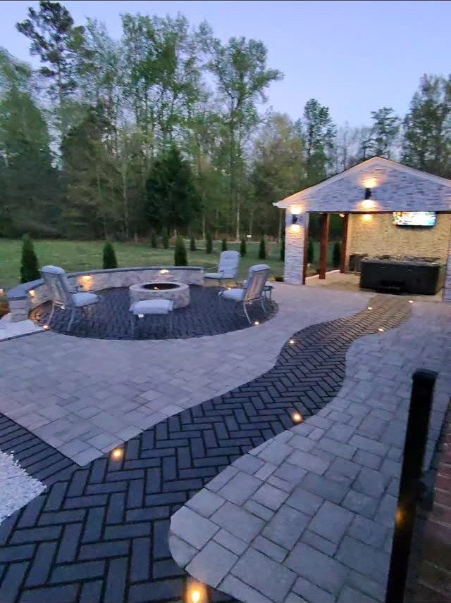 A large stone paver patio with a central fire pit and decorative herringbone patterns.