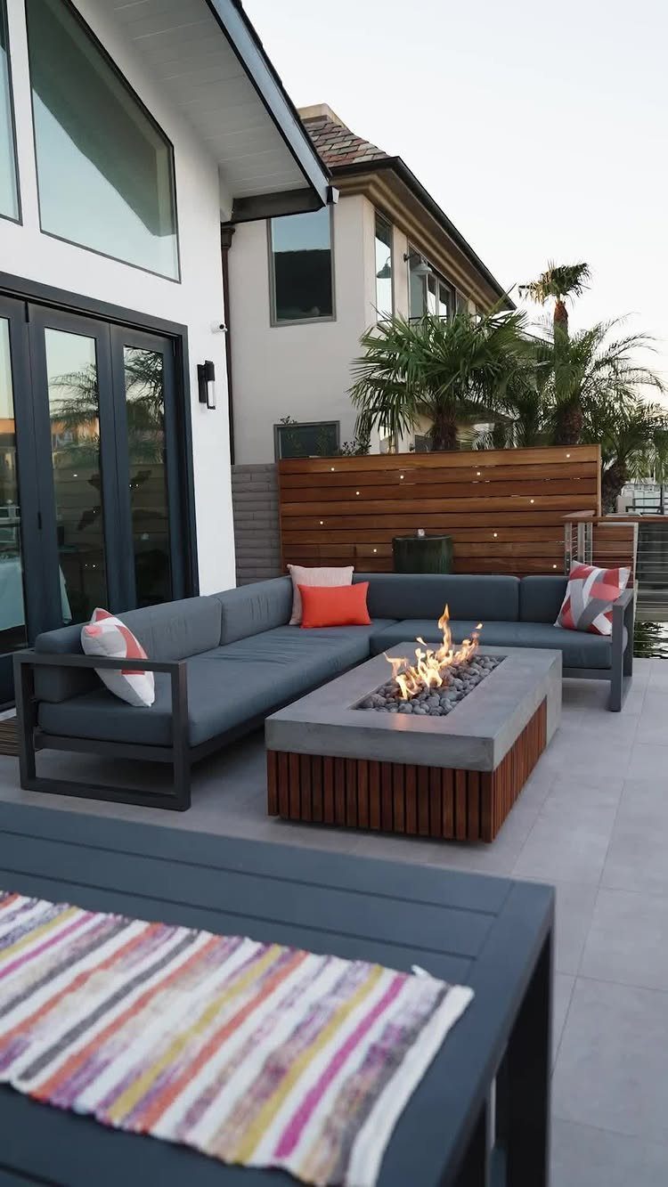 Modern rectangular gas fire pit table with a stone top and wooden base on a patio.