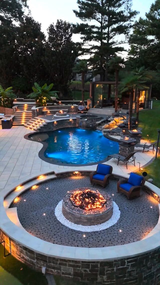 A circular sunken fire pit lounge with blue chairs and a swimming pool in the background.