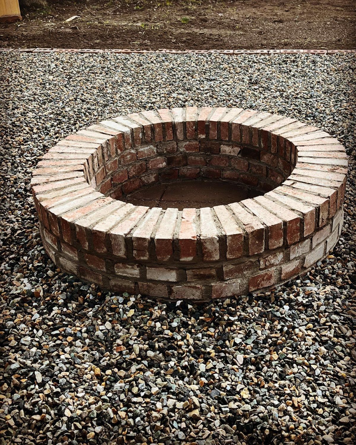 A circular brick fire pit sits centered on a bed of grey gravel.