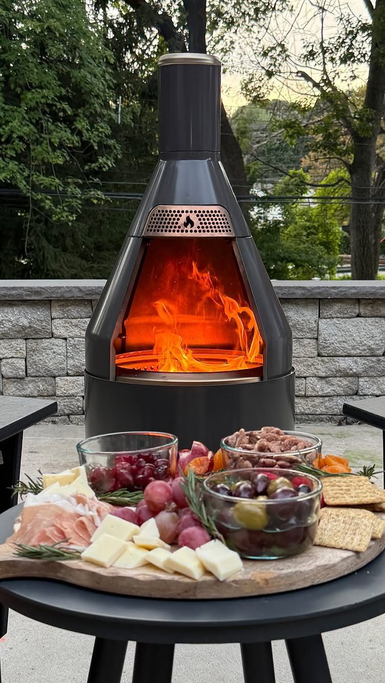 A black metal chiminea with a bright fire burning inside on an outdoor patio.