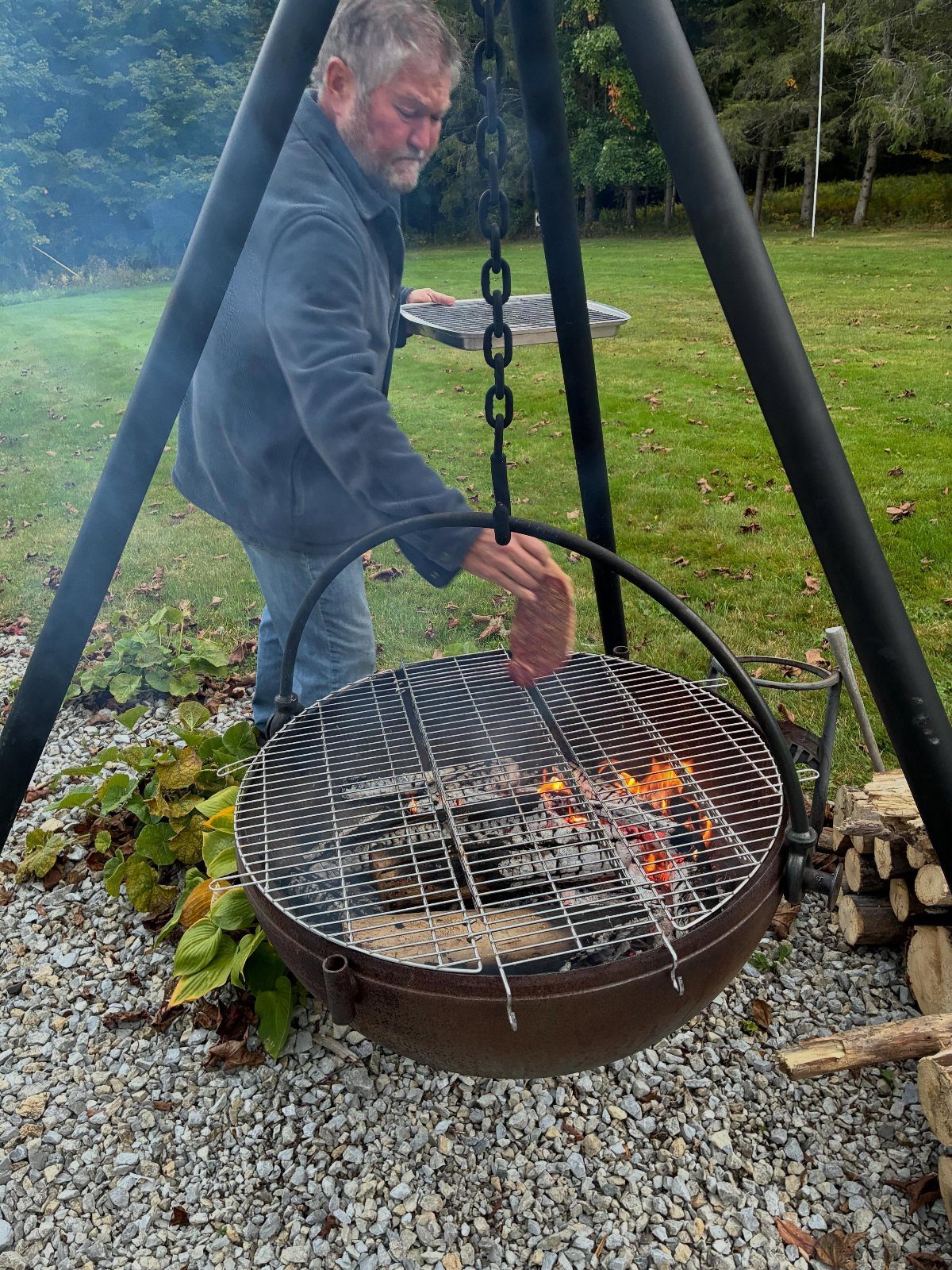 Man cooking food over a large metal cauldron fire pit suspended by a tripod.