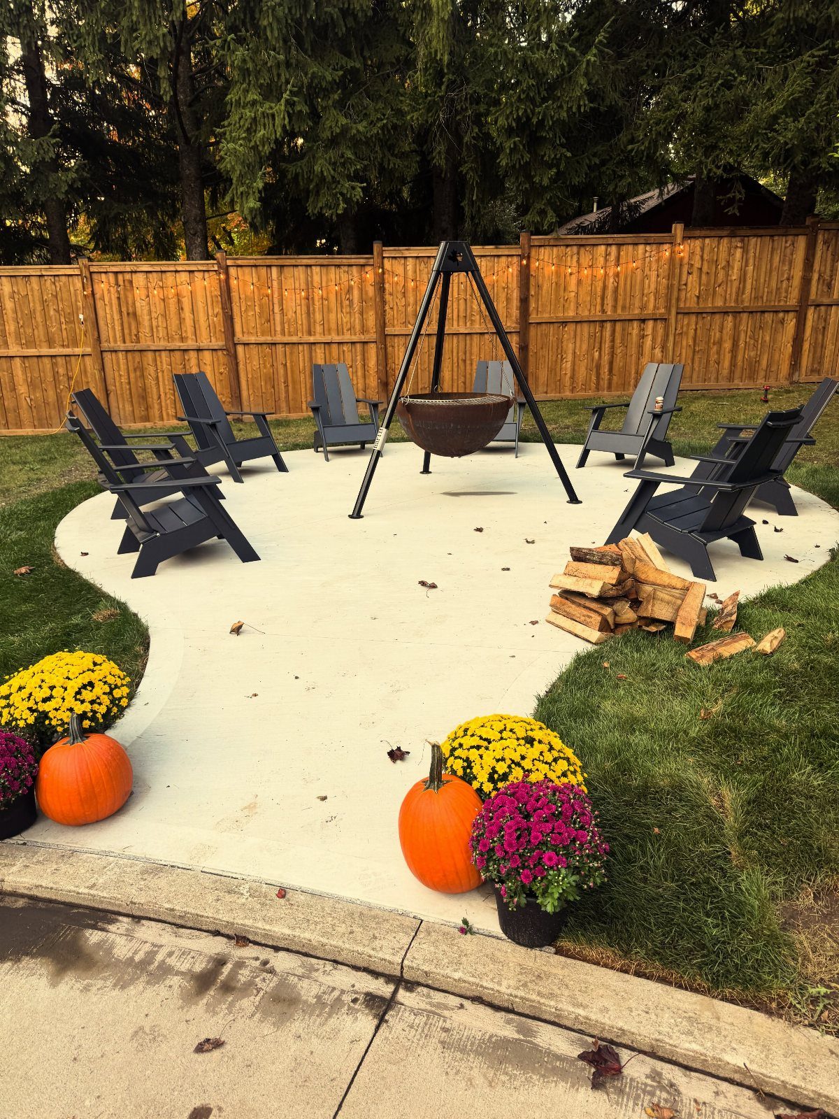 Dark grey Adirondack chairs arranged around a hanging fire bowl on a concrete patio.