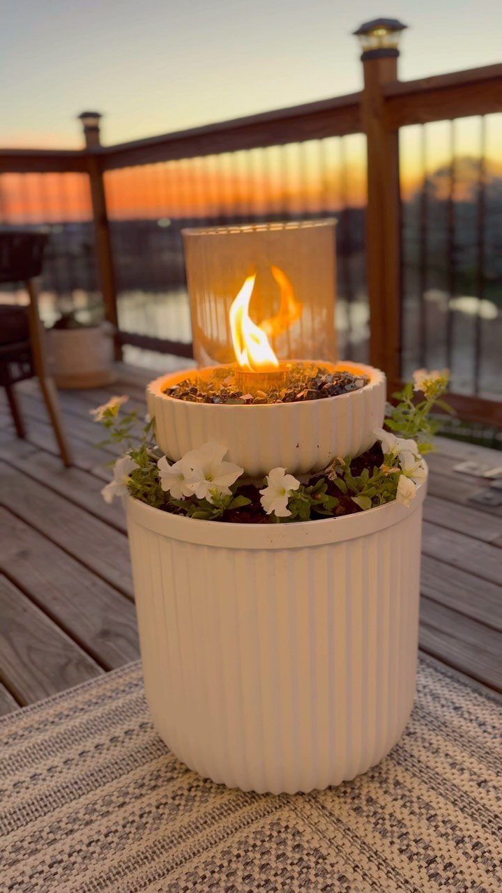 A white ribbed planter with small white flowers and a central flame inside a glass cylinder.