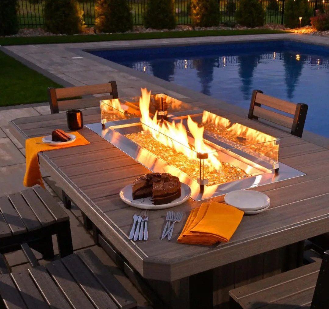 A rectangular gas fire pit with yellow flames integrated into a wooden outdoor dining table.