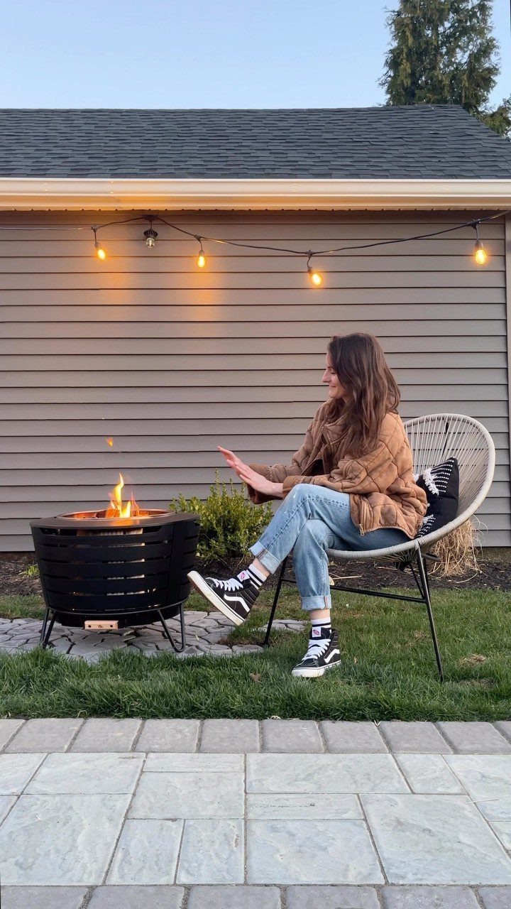 A woman sitting in a chair warming her hands by a portable black metal fire pit.