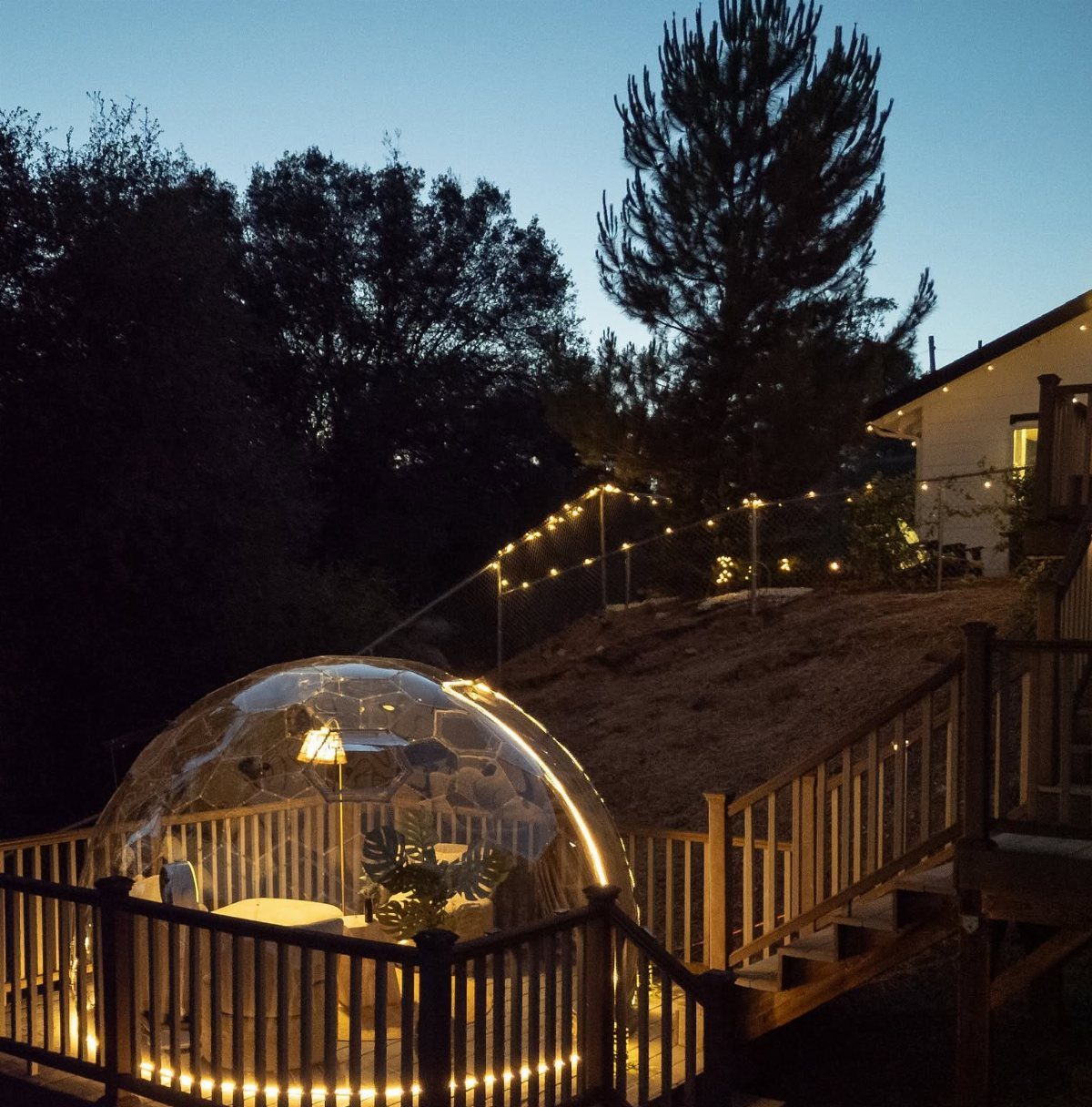 23 Backyard Garden Inspiration Ideas for Any Space 20 A glowing bubble tent containing a dining set sits on a wooden deck at twilight.