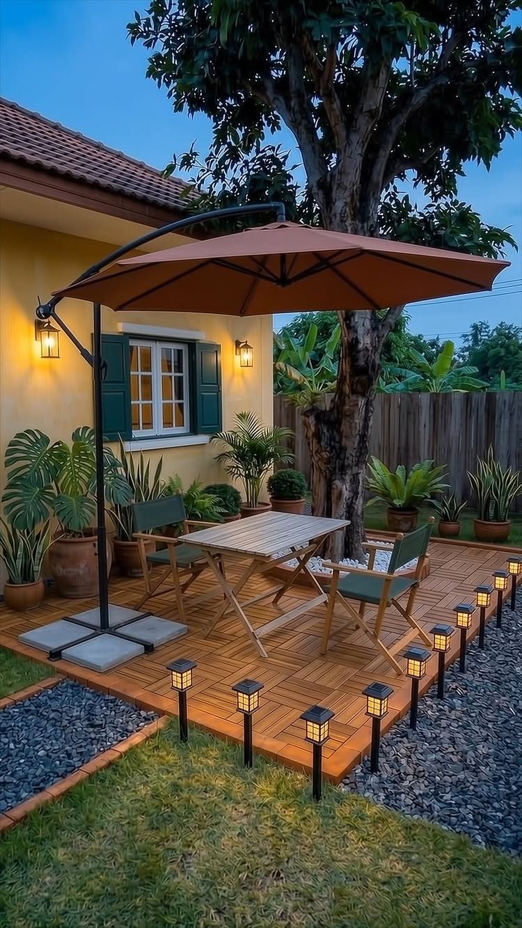 23 Backyard Garden Inspiration Ideas for Any Space 1 Wooden deck with dining furniture under a large brown umbrella, bordered by solar lights and gravel.