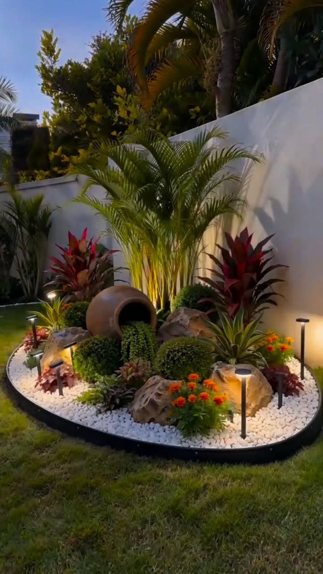 23 Backyard Garden Inspiration Ideas for Any Space 11 A landscaped garden bed featuring tropical plants, large rocks, and a decorative terracotta pot.