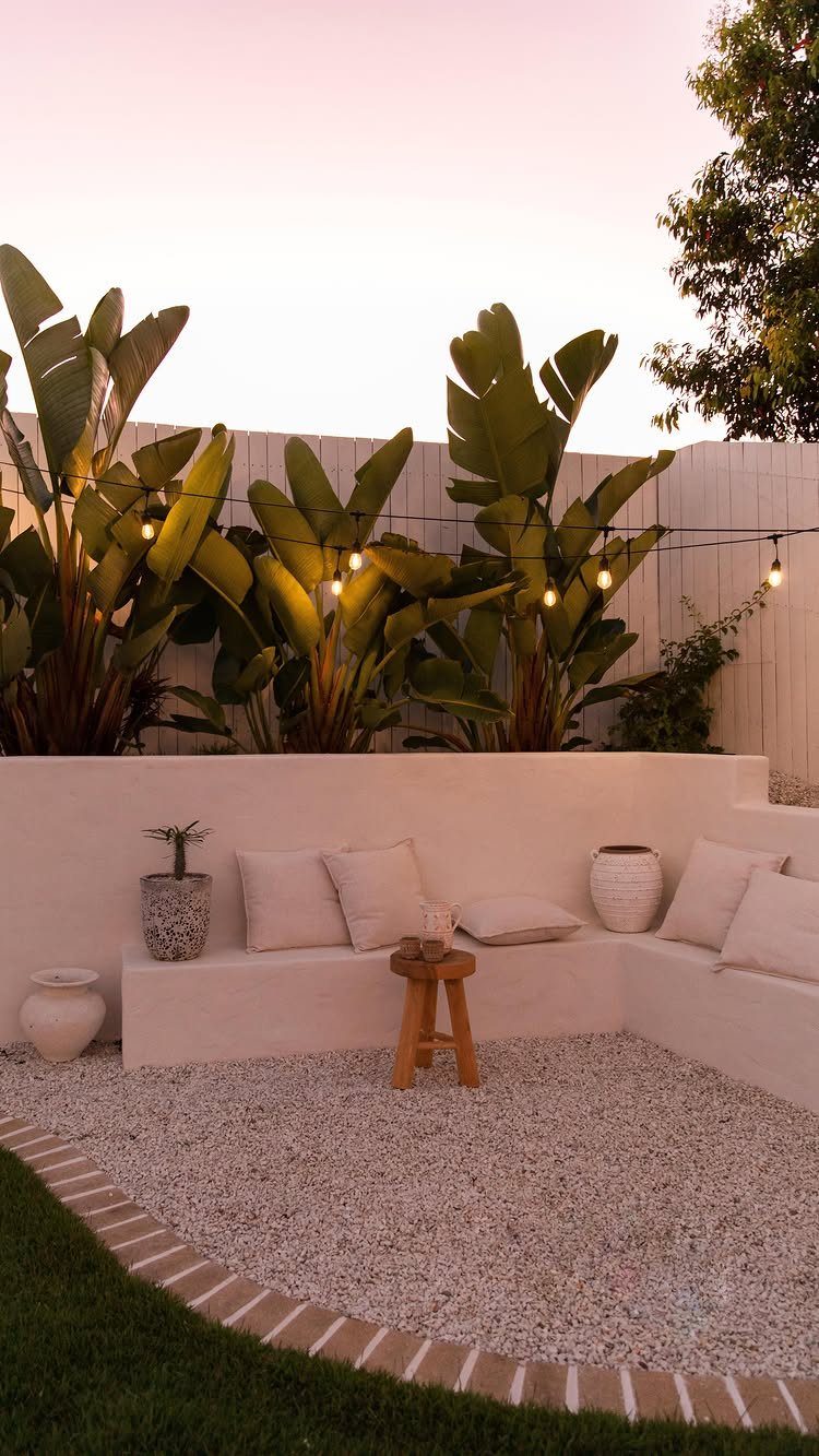 23 Backyard Garden Inspiration Ideas for Any Space 5 White stucco retaining wall used as a built-in garden bench with pillows and gravel.