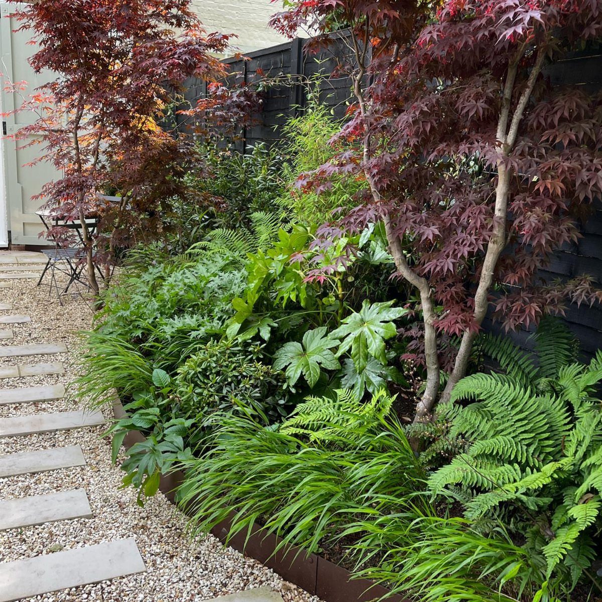 23 Backyard Garden Inspiration Ideas for Any Space 13 Green ferns and reddish Japanese maple trees planted in a lush garden bed.