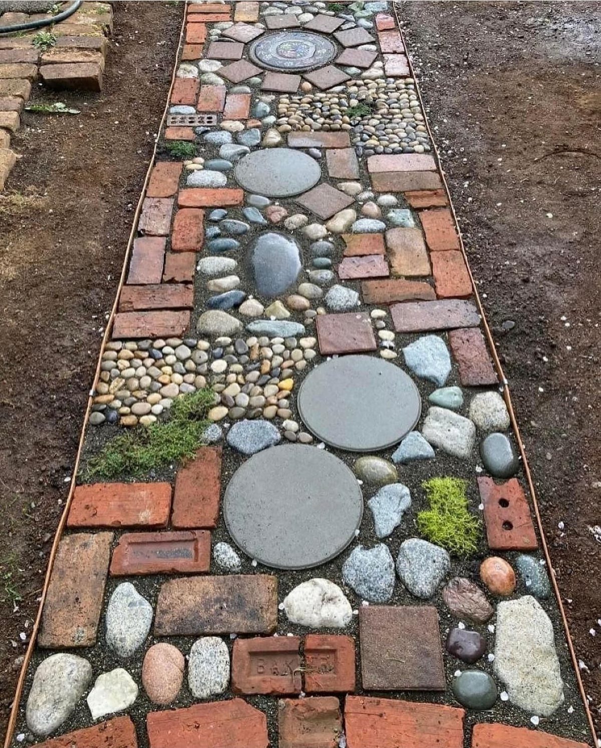 A mosaic garden path composed of red bricks, pebbles, and large circular grey stepping stones.