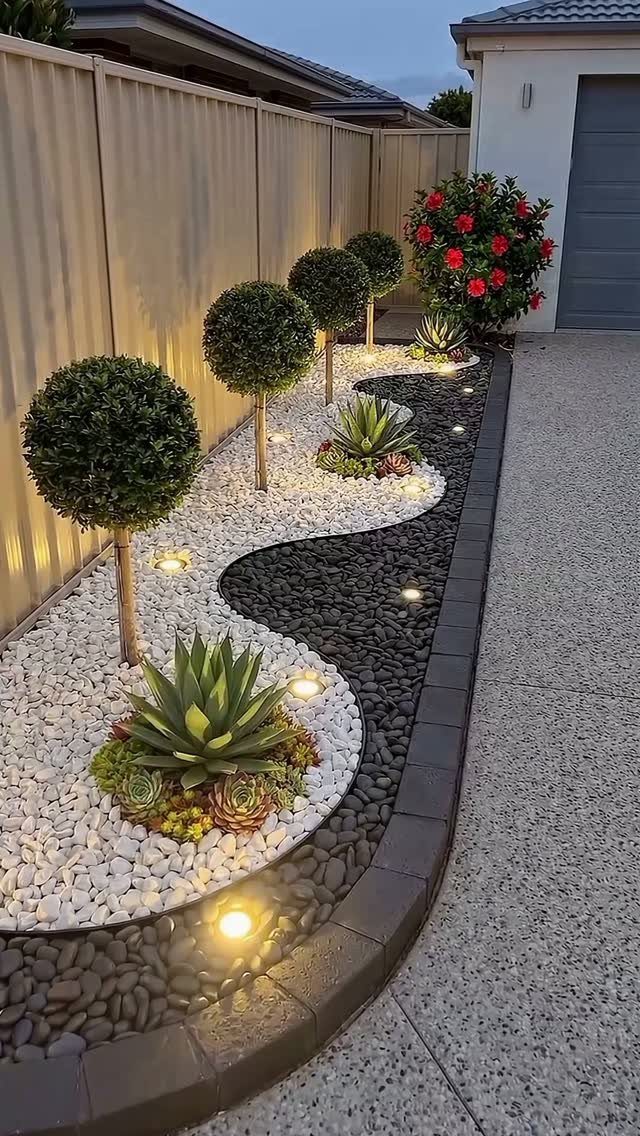 Manicured trees and succulents planted in white and black pebble beds with landscape lighting.