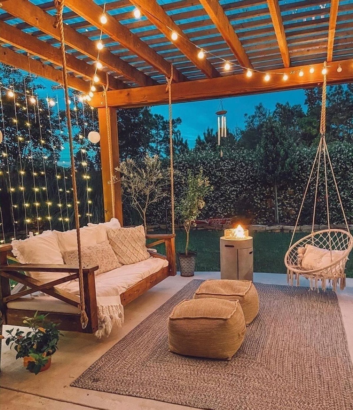 9 Backyard Patio Ideas with Fire Pits, Shade Sails & Retractable Awnings 5 A cozy backyard patio at dusk with string lights, a wooden swing bench, and a hanging chair.
