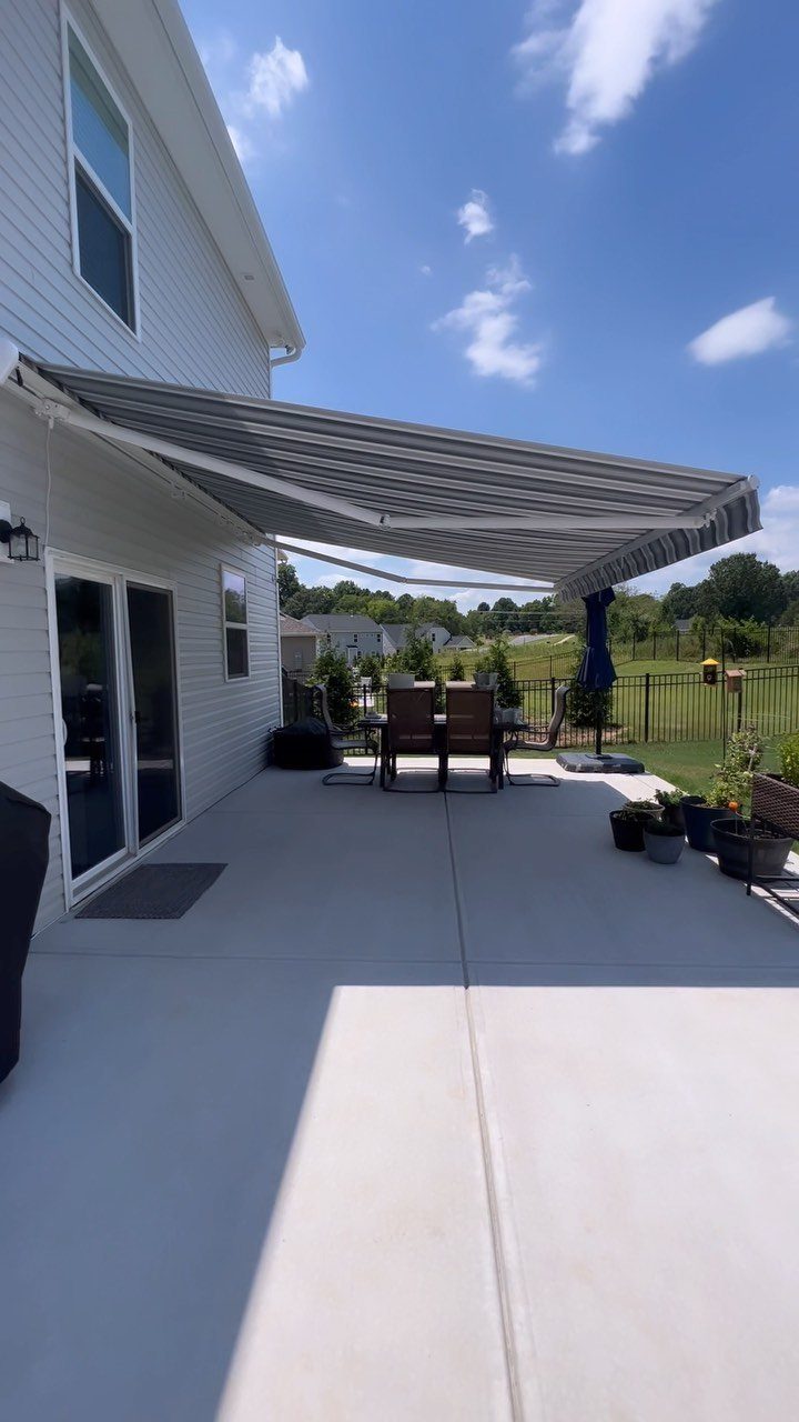 9 Backyard Patio Ideas with Fire Pits, Shade Sails & Retractable Awnings 9 A striped retractable awning provides shade over a concrete patio and outdoor dining set.