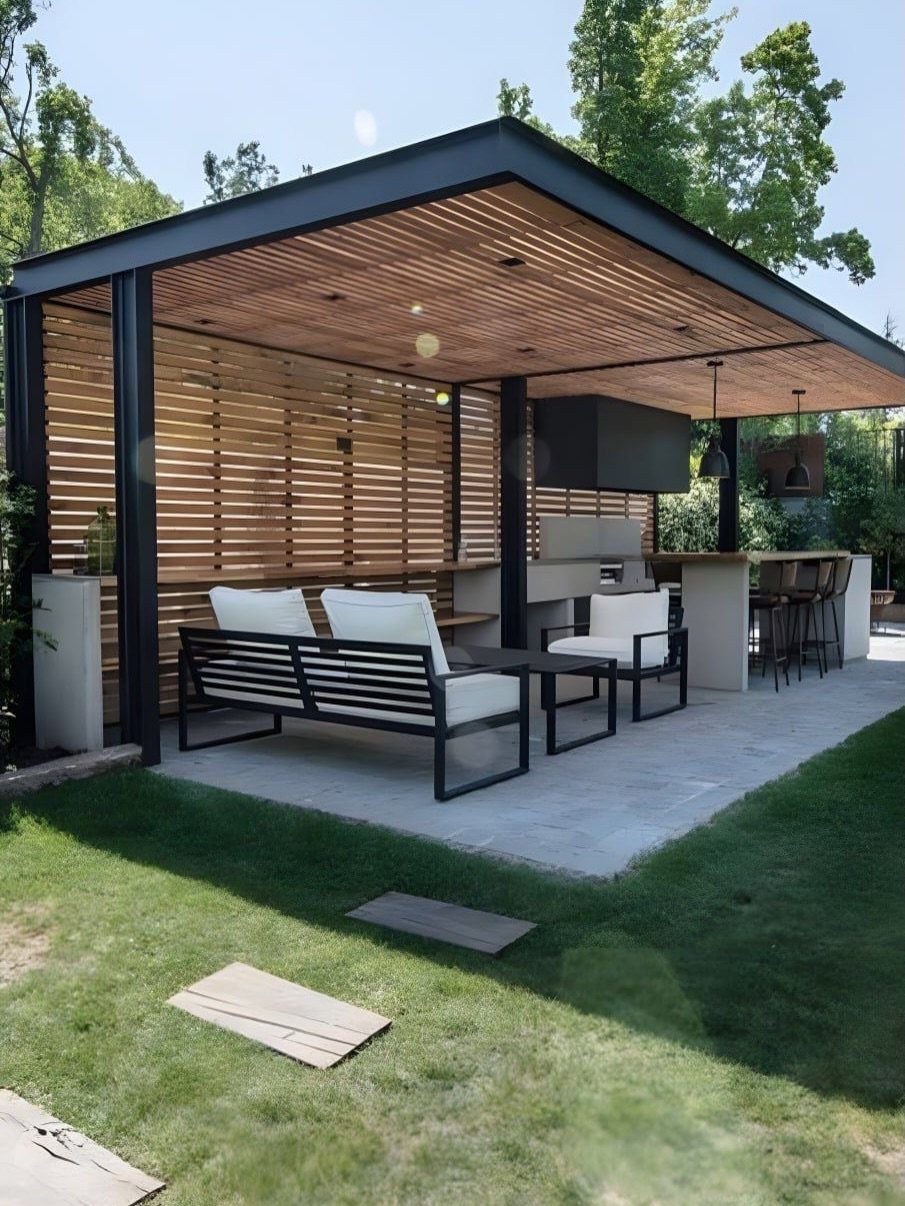 Modern outdoor pavilion with wooden slatted ceiling and white lounge furniture on a stone patio.