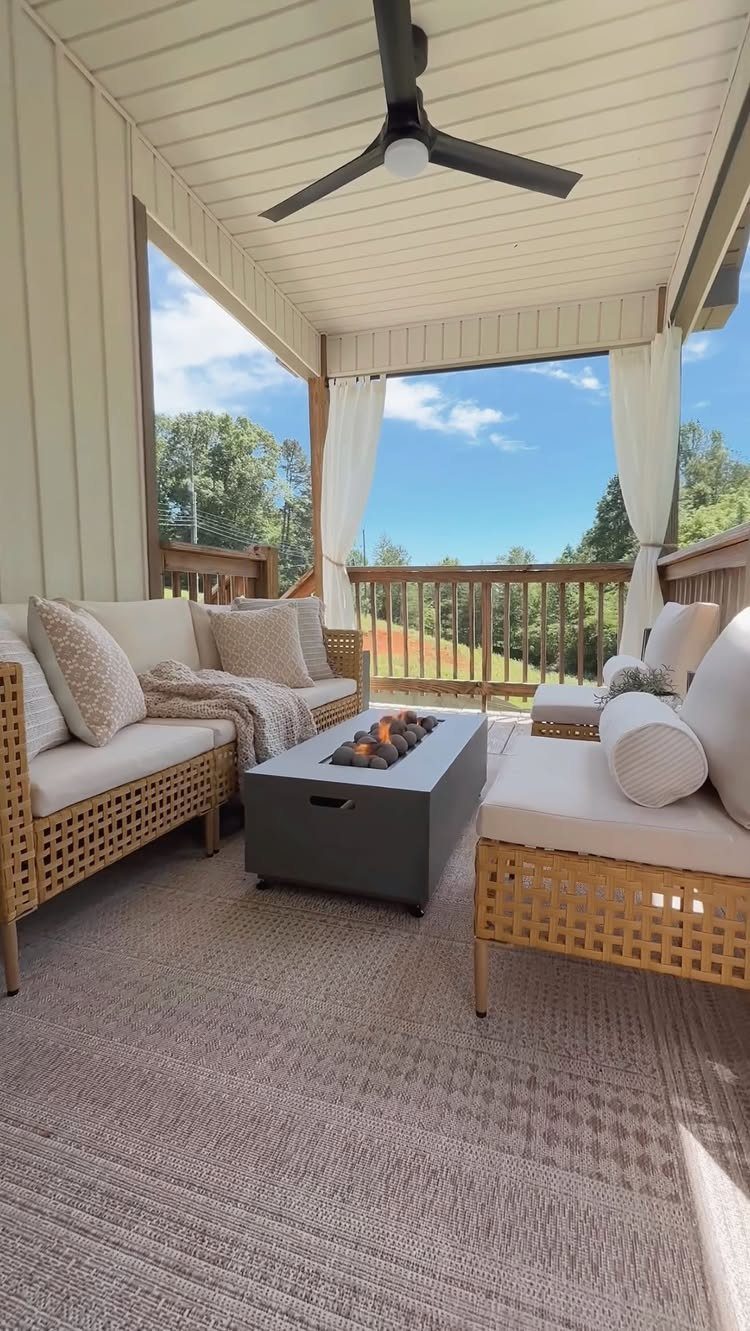 White outdoor curtains hanging from a covered patio structure overlooking a green landscape.