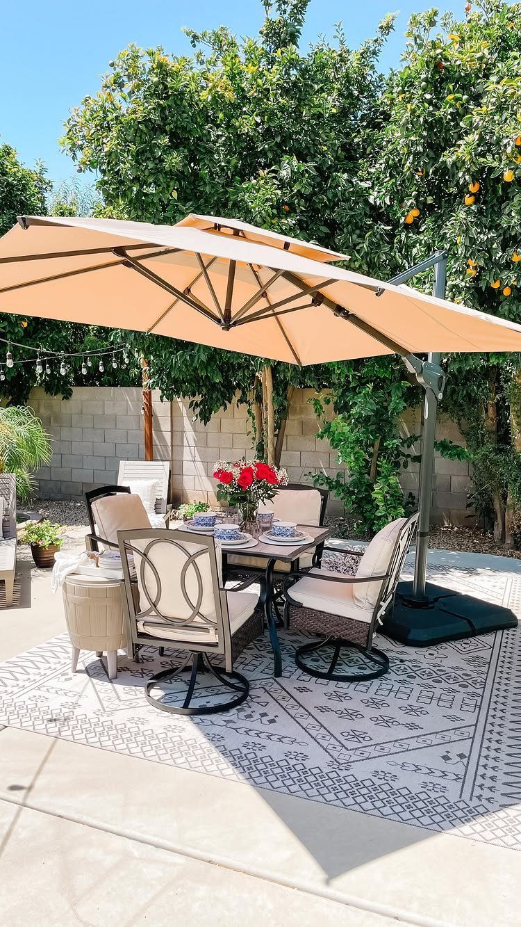 A large tan cantilever umbrella shading a patio dining set on a patterned rug.