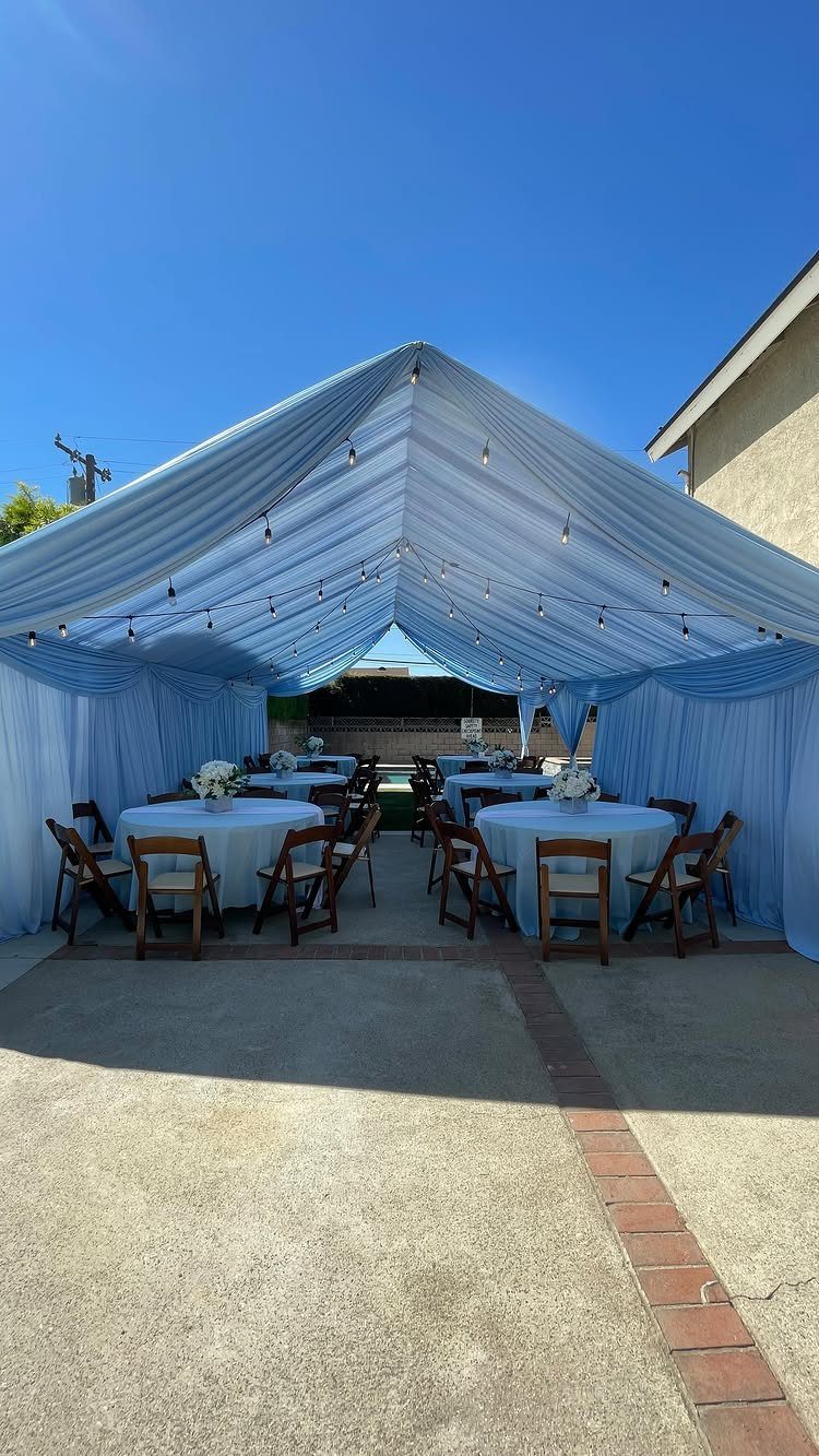Light blue event tent set up with round tables and wooden chairs on a patio.