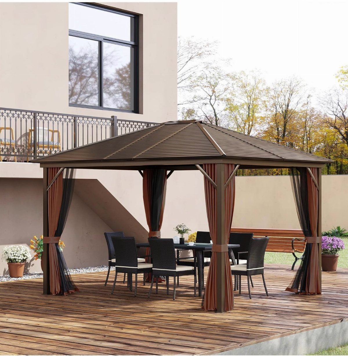 A dark brown metal gazebo with orange curtains sits on a wooden deck with dining furniture.