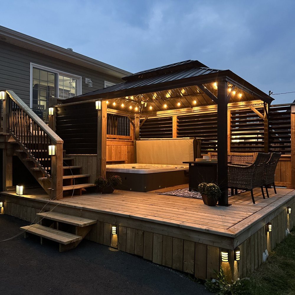 Wooden gazebo with string lights housing a hot tub on a large backyard deck.