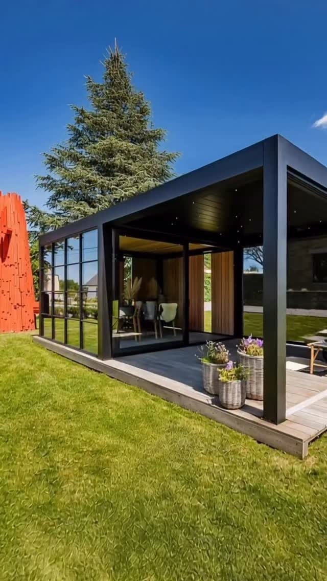 Modern black metal outdoor structure with glass walls on a wooden deck in a grassy yard.