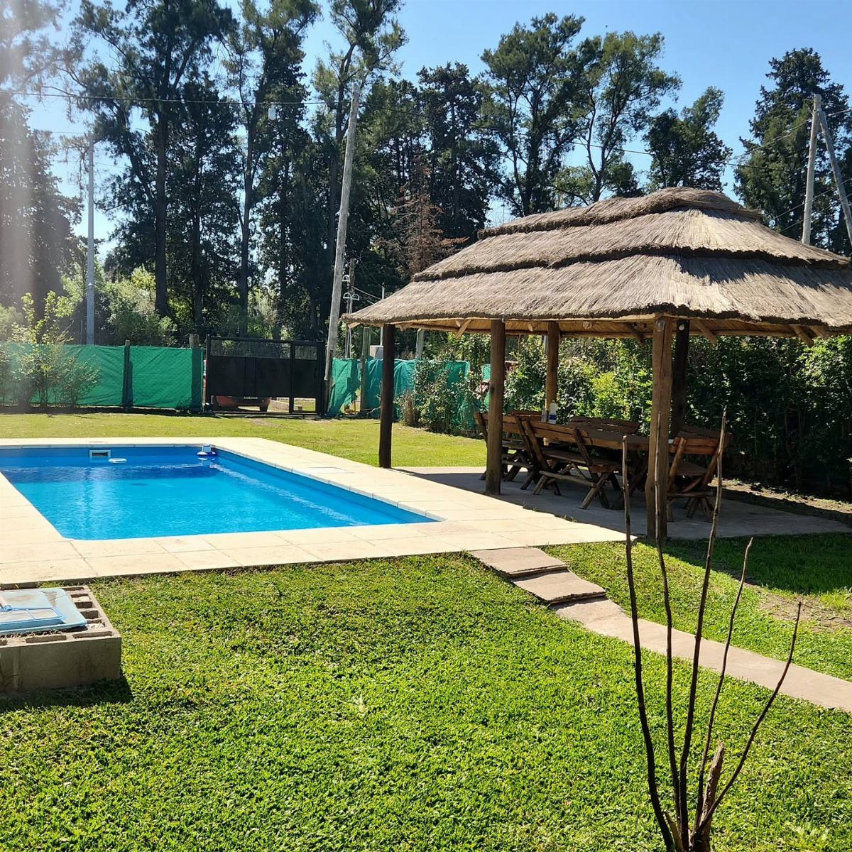 A thatched roof wooden gazebo situated on a lawn next to a bright blue swimming pool.