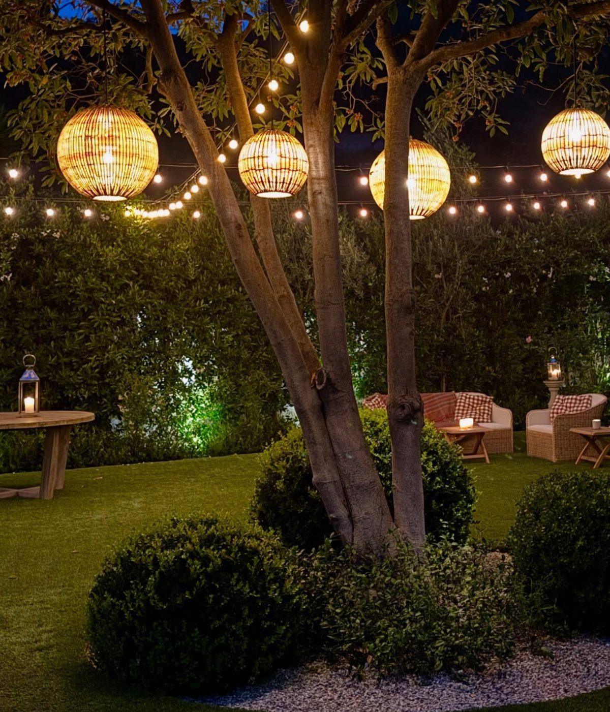 16 Beautiful Backyard Ideas for Cozy to Elegant Outdoor Spaces 2 Glowing spherical lanterns and string lights hanging from tree branches in a dark, lush backyard.