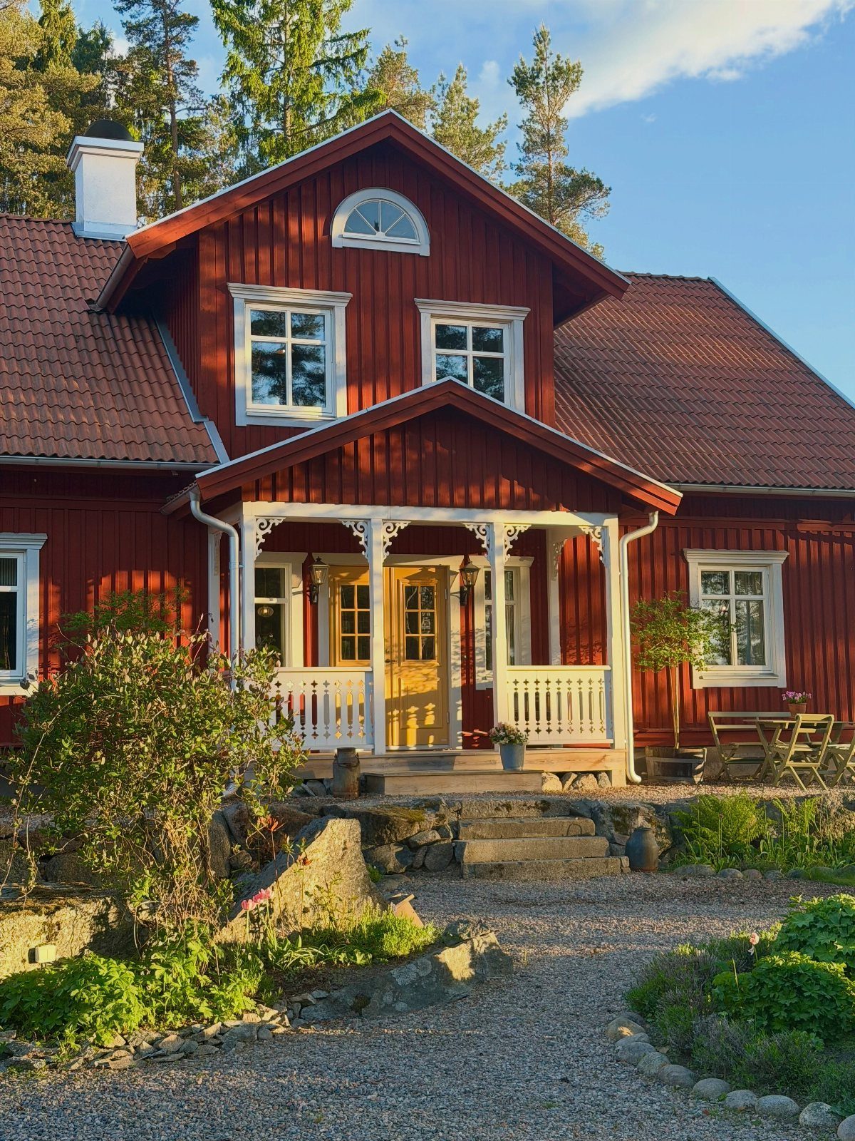 A red wooden farmhouse with white trim, a small porch, and a gravel garden path.