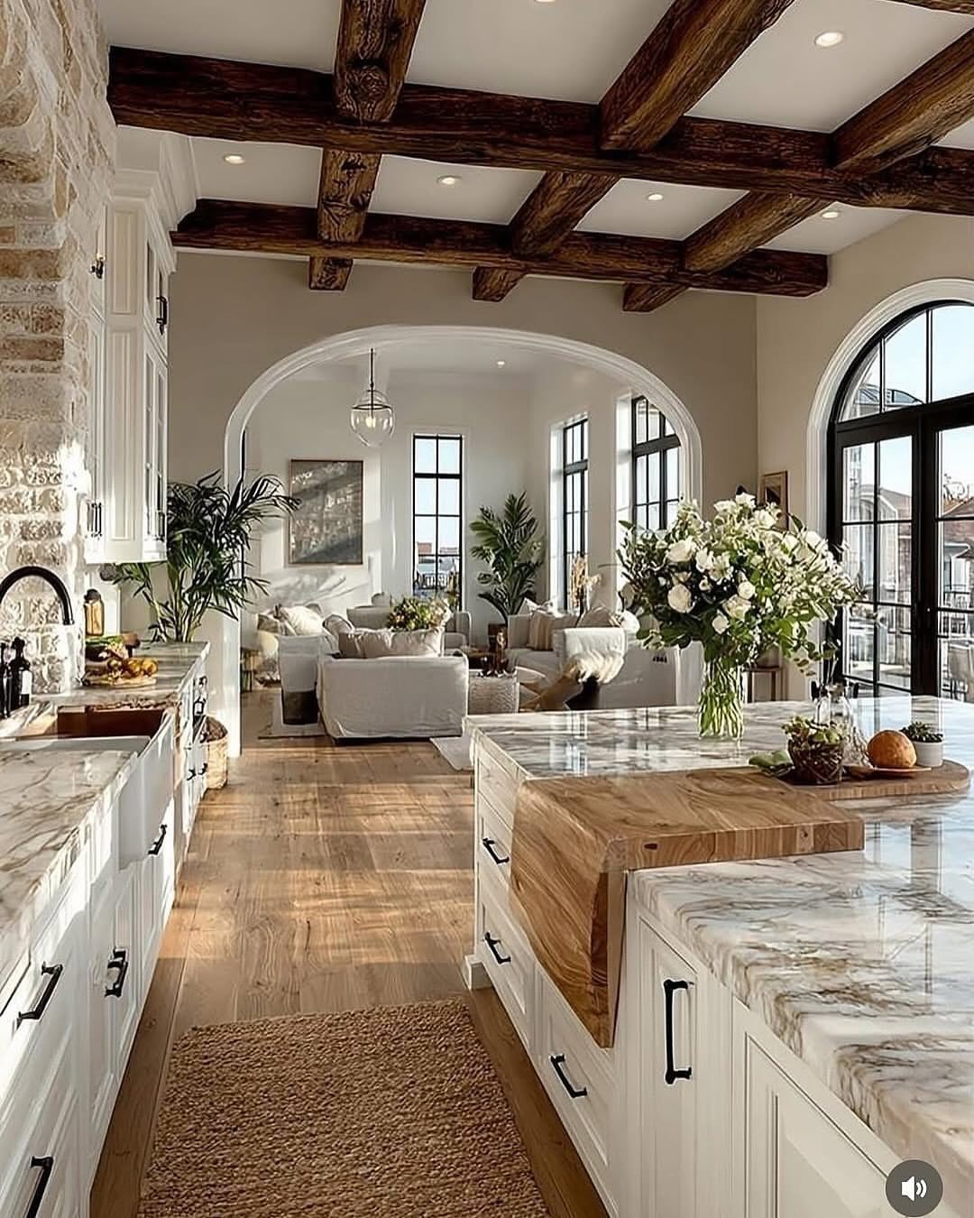 Rustic interior with dark wooden ceiling beams, marble countertops, and white cabinetry in an open living space.