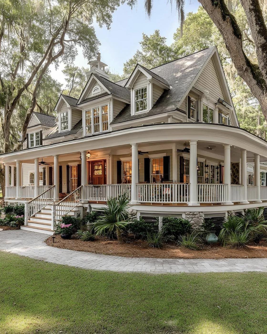 A large beige farmhouse featuring a wide white wraparound porch and multiple gabled dormer windows.