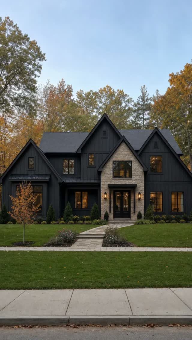 16 Black Modern Farmhouse Exterior Ideas With Photos 12 A black modern farmhouse with stone accents and a green lawn under autumn trees.