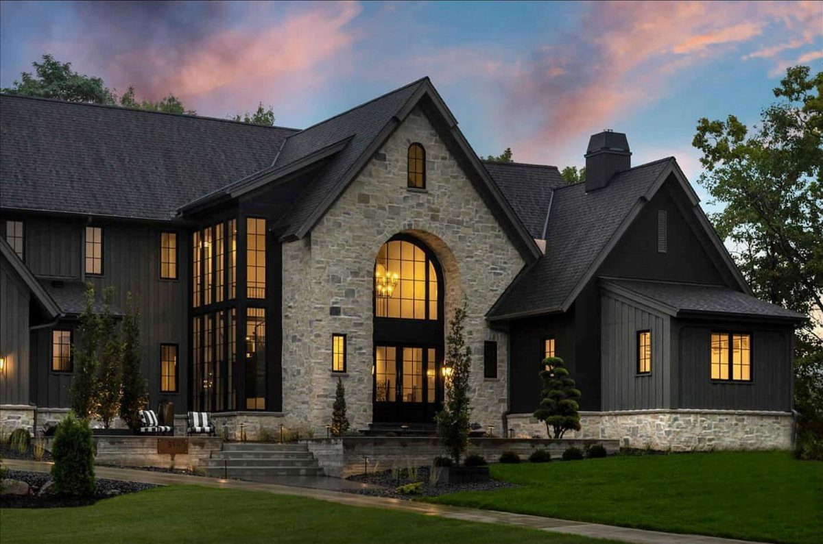 16 Black Modern Farmhouse Exterior Ideas With Photos 5 Modern black farmhouse with stone facade and large arched glass windows at twilight.