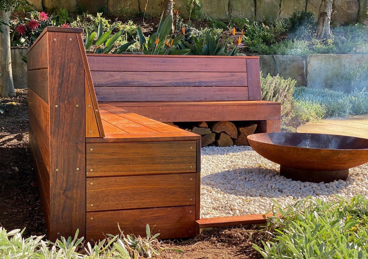 A custom cedar wood bench with integrated seating surrounding a metal fire bowl on white pebbles.